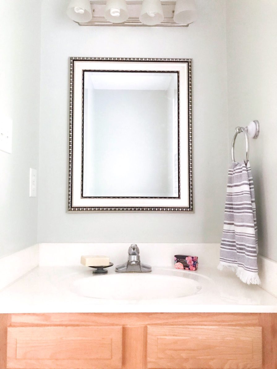 builder grade bathroom with new mirror and Sherwin Williams Sea Salt painted walls