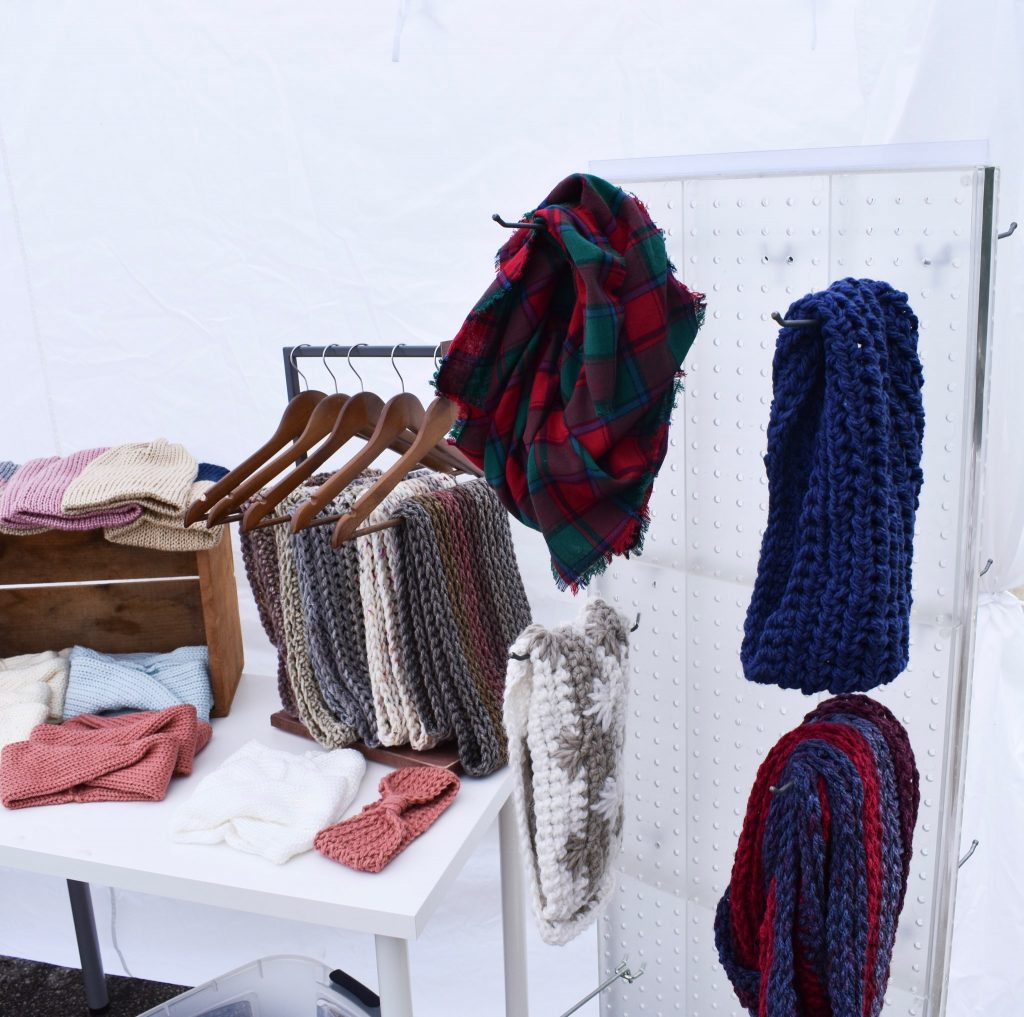 handmade knit scarves hanging on wooden hangers at a craft fair