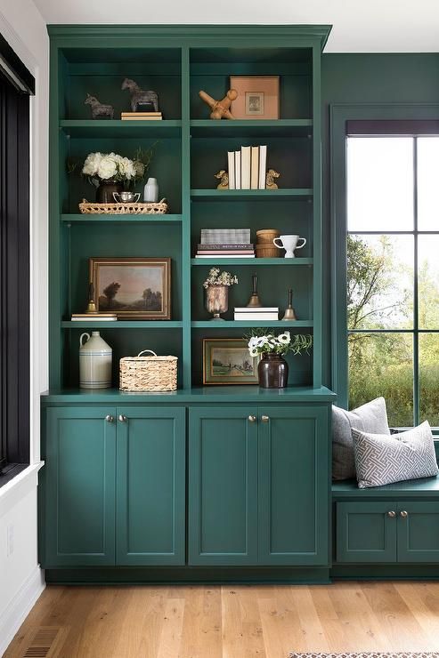 Home office with green built in bookcases and a window seat.