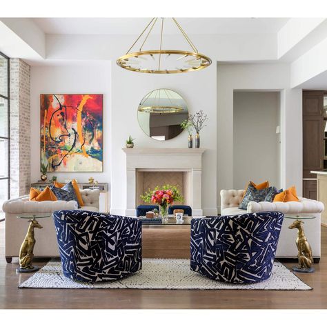 Living room with two off-white sofas and two graphic blue chairs paired with brass whippet statue and glass side tables.